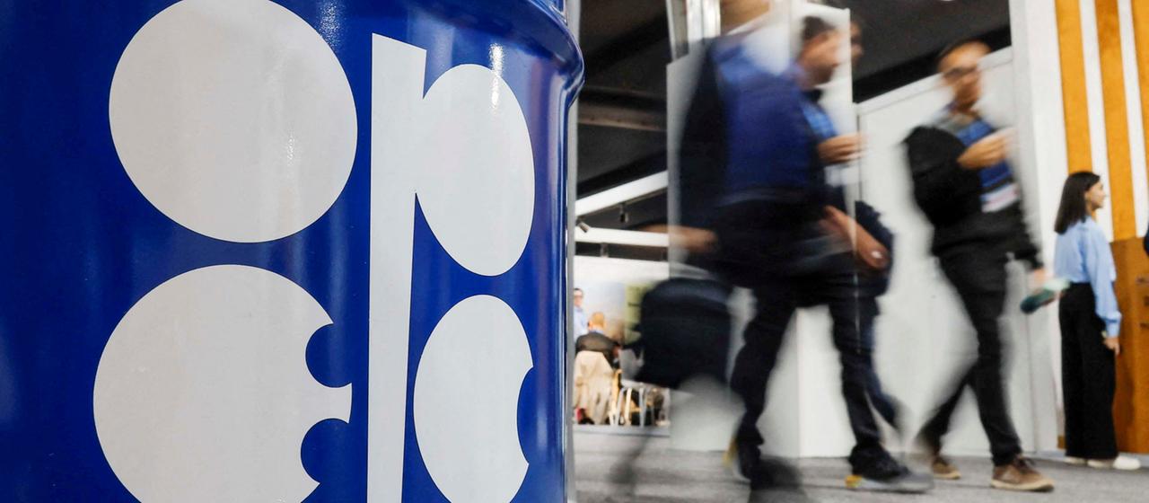 Menschen gehen an einem Ölfass mit der Aufschrift "OPEC" vorbei.