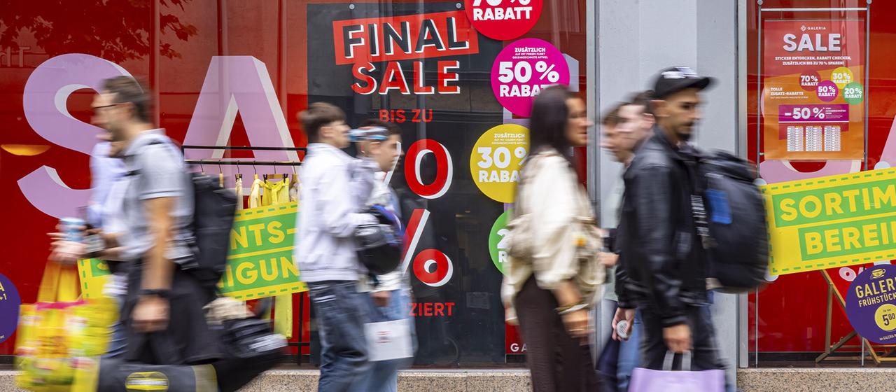 Passanten laufen mit Einkaufstüten an einem Schaufenster vorbei.