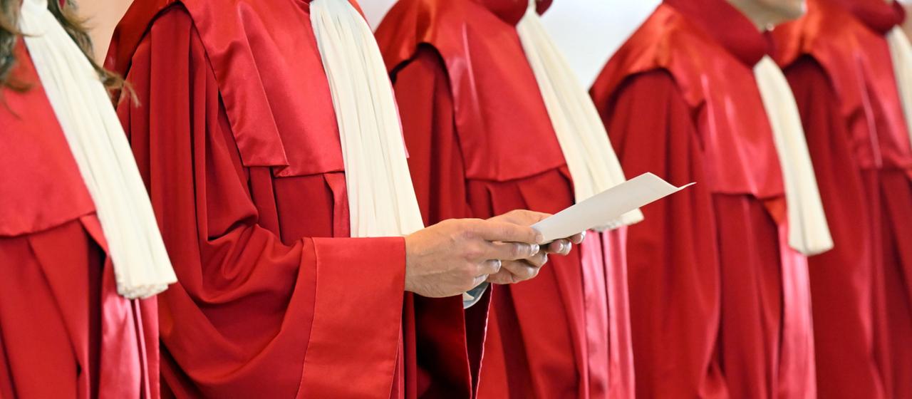 Richter stehen in roten Roben vor einem Tisch, ihre Köpfe sind nicht zu shen.