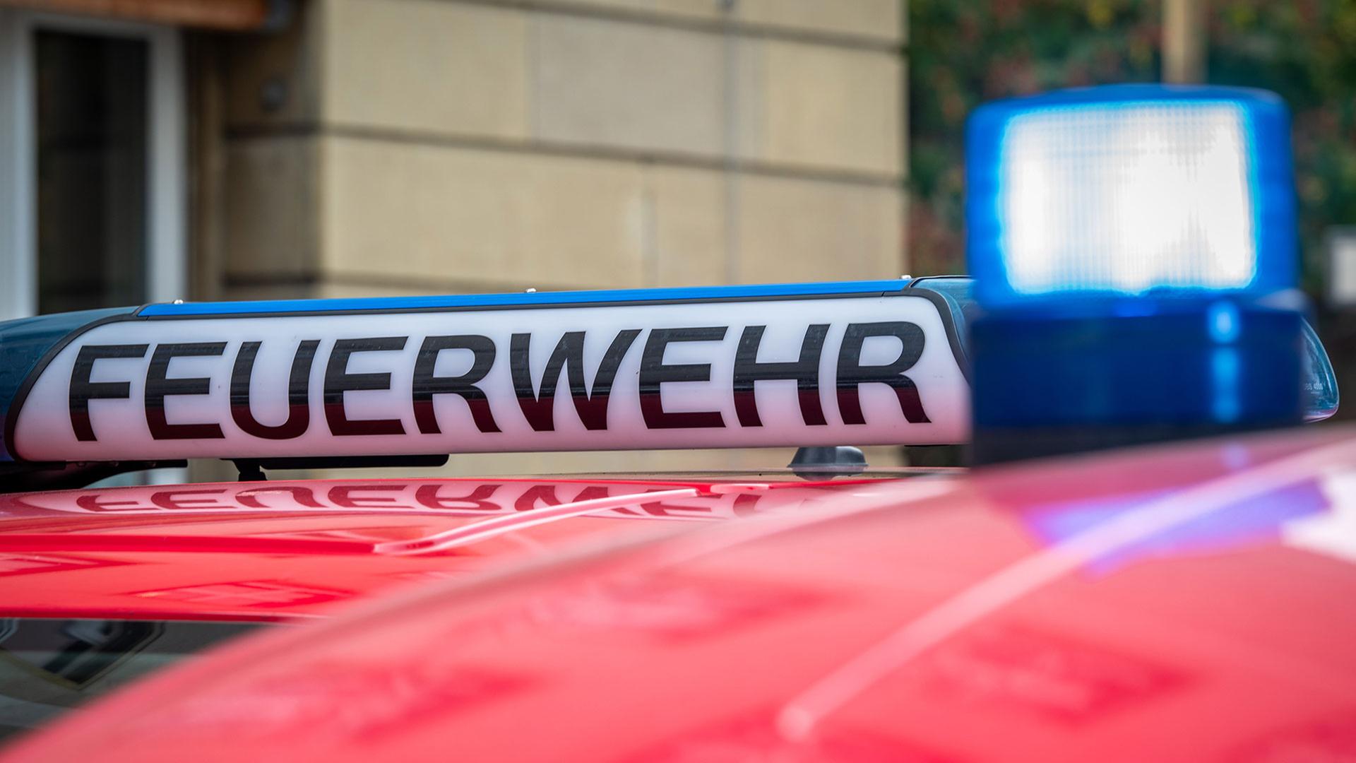 Der Schriftzug „Feuerwehr“ ist neben einem blau leuchtenden Sondersignal auf dem Dach eines Fahrzeuges der Feuerwehr zu sehen. | picture alliance/dpa | Soeren Stache