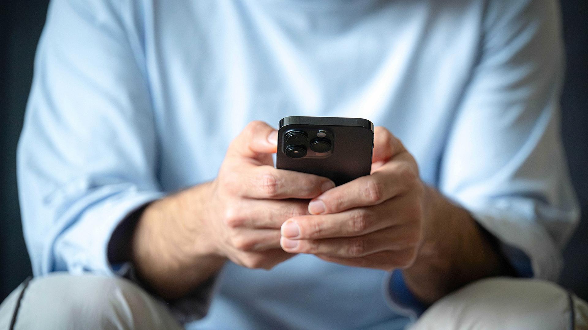Ein Mann tippt auf ein Mobiltelefon. | dpa