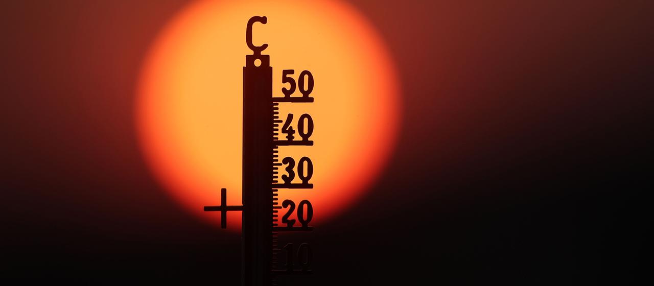 Hinter einem Thermometer geht am Morgen die Sonne auf.