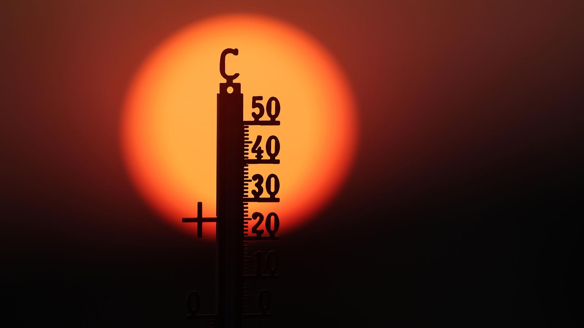 Hinter einem Thermometer geht am Morgen die Sonne auf. | Thomas Warnack/dpa