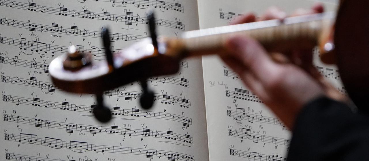 Eine Person spielt Geige, im Hintergrund ein Notenblatt.