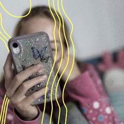 Ein Maedchen sitzt in ihrem Bett und ist am Handy.