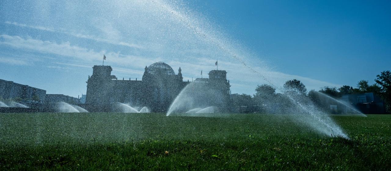 Starhlende Sonne und mehrer Rasensprenger vor dem Bundestag in Berlin
