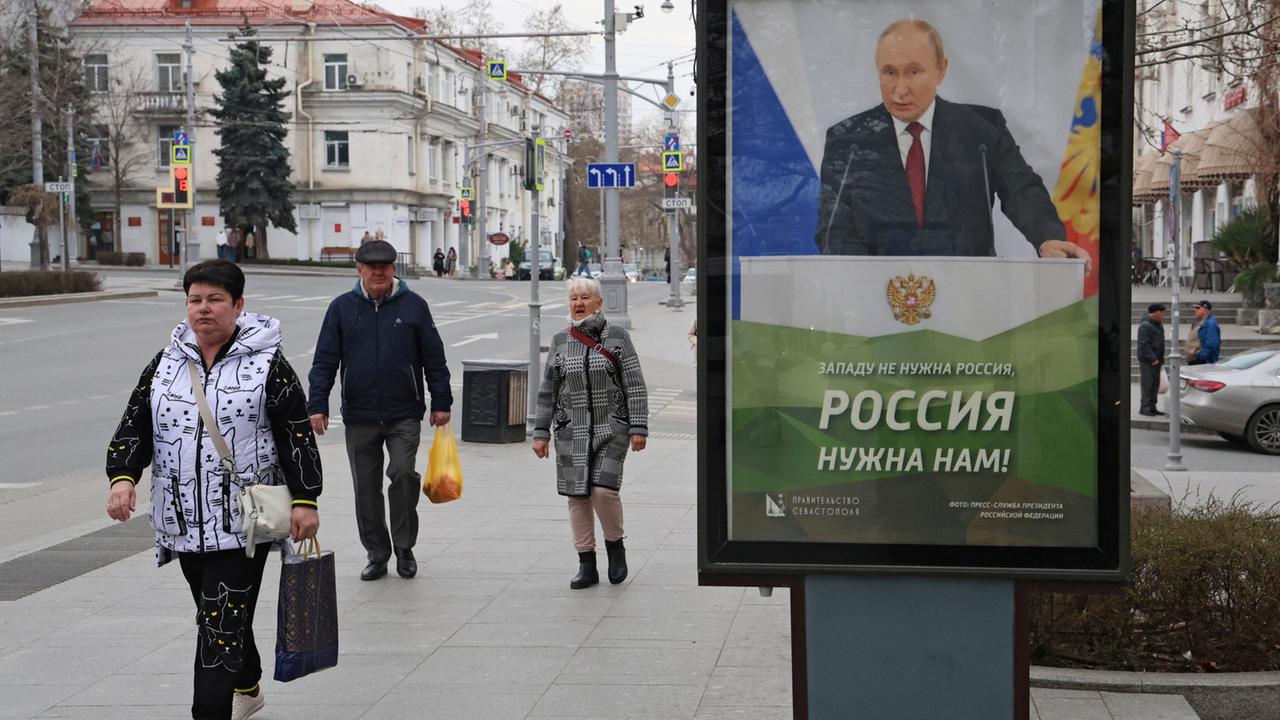 Passanten laufen auf der Krim an einem Plakat des russischen Präsidenten Wladimir Putin vorbei. | REUTERS