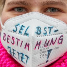 Eine Person trägt bei einer Demonstration eine FFP2-Maske mit der Aufschrift "Selbstbestimmung Jetzt!"