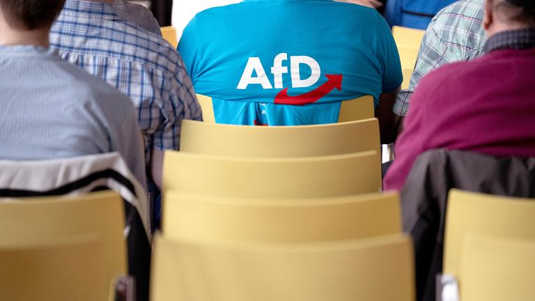 Ein Mann mit einem T-Shirt mit AfD-Logo sitzt während des Landesparteitags der Alternative für Deutschland Hessen im Haus der Begegnung im Publikum. 