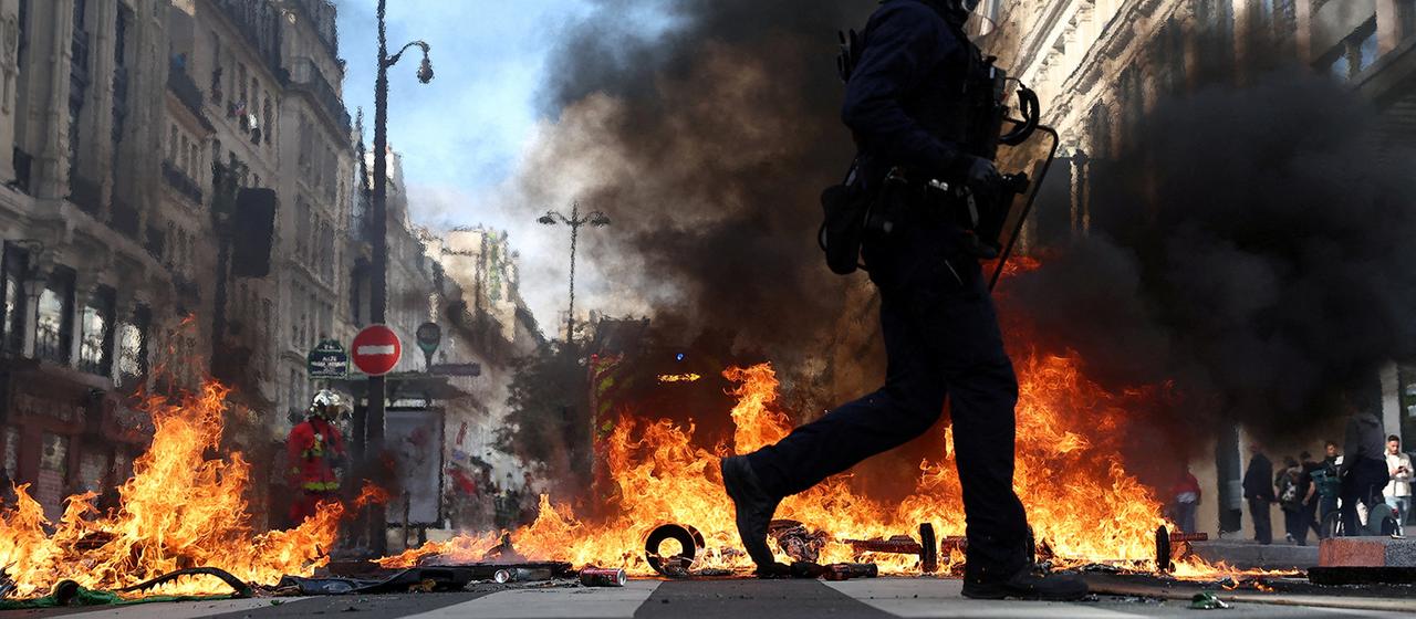 Ein Polizist geht an brennenden Gegenständen auf einer Straße in Paris vorbei.