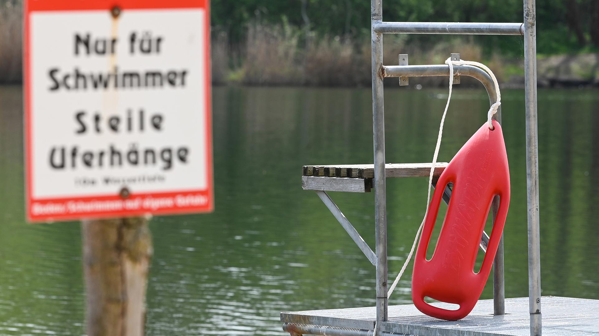 Eine Rettungsboje für den Schwimmmeister und ein Hinweisschild am Strand des Heidebades in Halle (Sachsen-Anhalt). | dpa