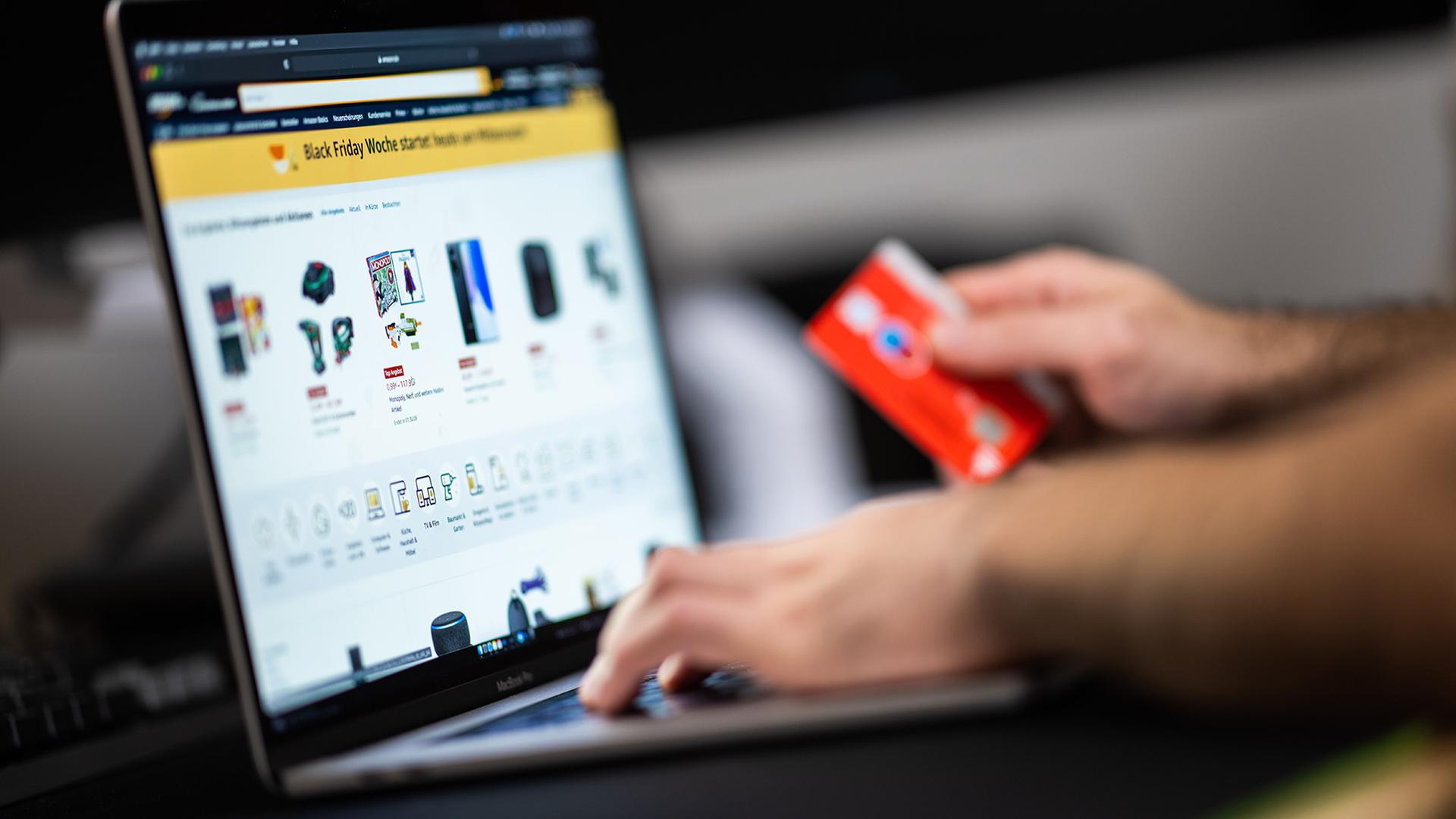 Eine Person sitzt mit einer Kreditkarte in der Hand vor einem Laptop. | picture alliance/dpa