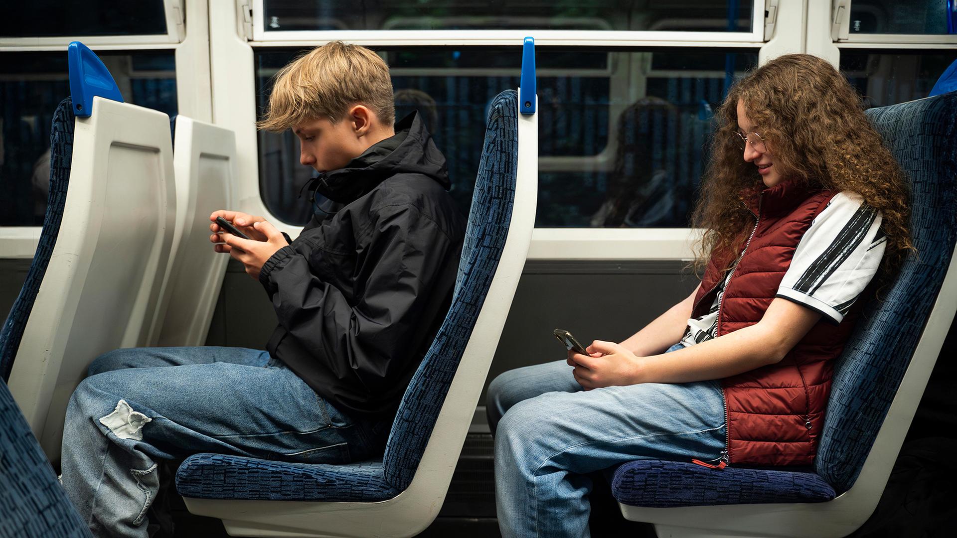 Ein Junge und ein Mädchen sitzen in einem Zug und gucke auf ihre Smartphones. | picture alliance / Westend61