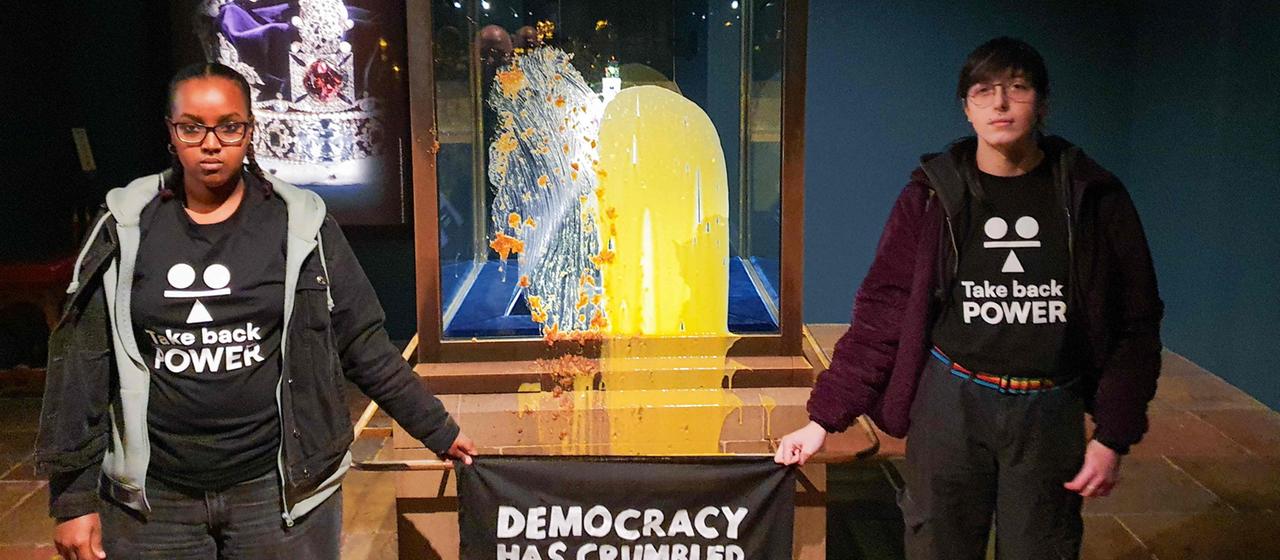 Protestierende halten ein Banner vor die beschmierte Vitrine.