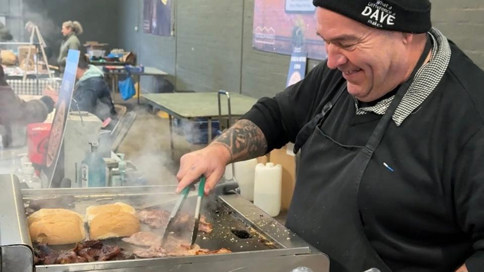 Dave Brent steht am Grill und bereitet Burger zu.