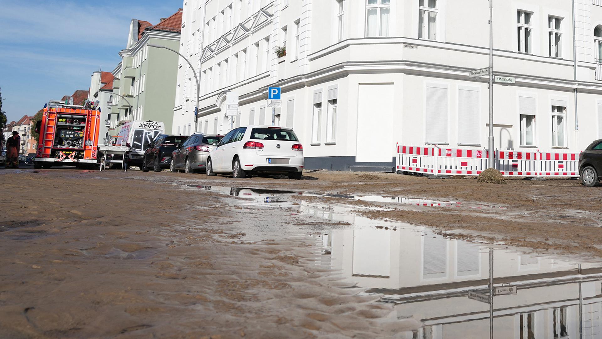 Feuerwehr, Matsch und eine Pfütze sind auf einer Straße nach einem Rohrbruch in Spandau zu sehen.(Quelle: picture alliance/dpa/Sven Kaeuler) | picture alliance/dpa/Sven Kaeuler
