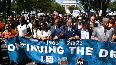 Teilnehmer einer Demonstration halten ein Transparent mit Aufschrift "1963-2023 Continuing the Dream"