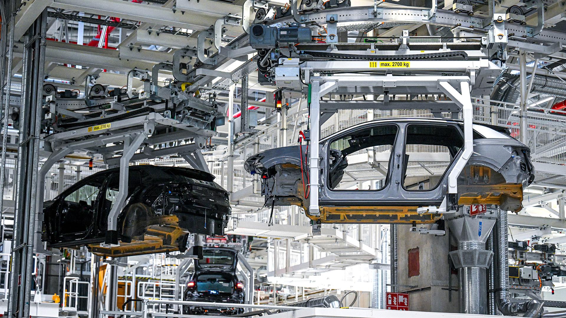 Fahrzeugkarosserien werden in einer Produktionshalle transportiert. | dpa