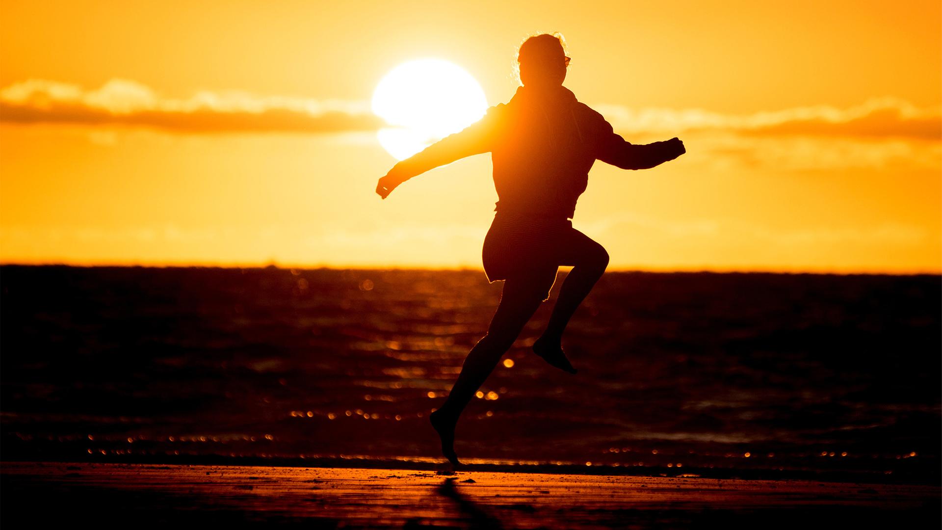 Ein Mädchen springt vor der untergehenden Sonne am Nordstrand im Sand.  | picture alliance/dpa