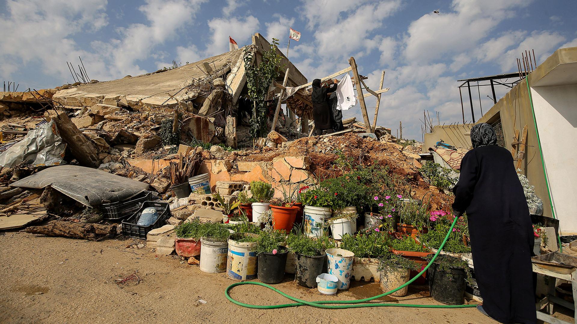 Eine Frau nimmt Wäsche ab, die auf einem Trümmerhaufen aufgehängt ist während eine andere Blumen gießt. | dpa