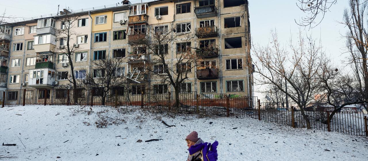 Eine Frau geht im ukrainischen Kiew in der Nähe eines zerstörten Wohnhauses vorbei.