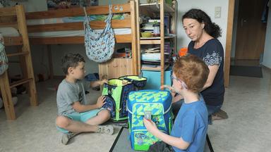 Eine Mutter sitzt mit ihren zwei Kindern vor zwei Hochbetten.