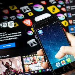 Eine Frau hält ein IPhone mit dem Appstore vor einem Bildschirm, auf dem der Epic Games Store zu sehen ist.