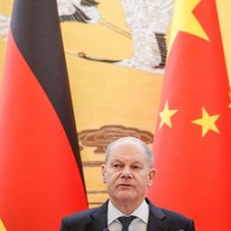 Olaf Scholz steht zwischen den Flaggen Deutschlands und Chinas. 