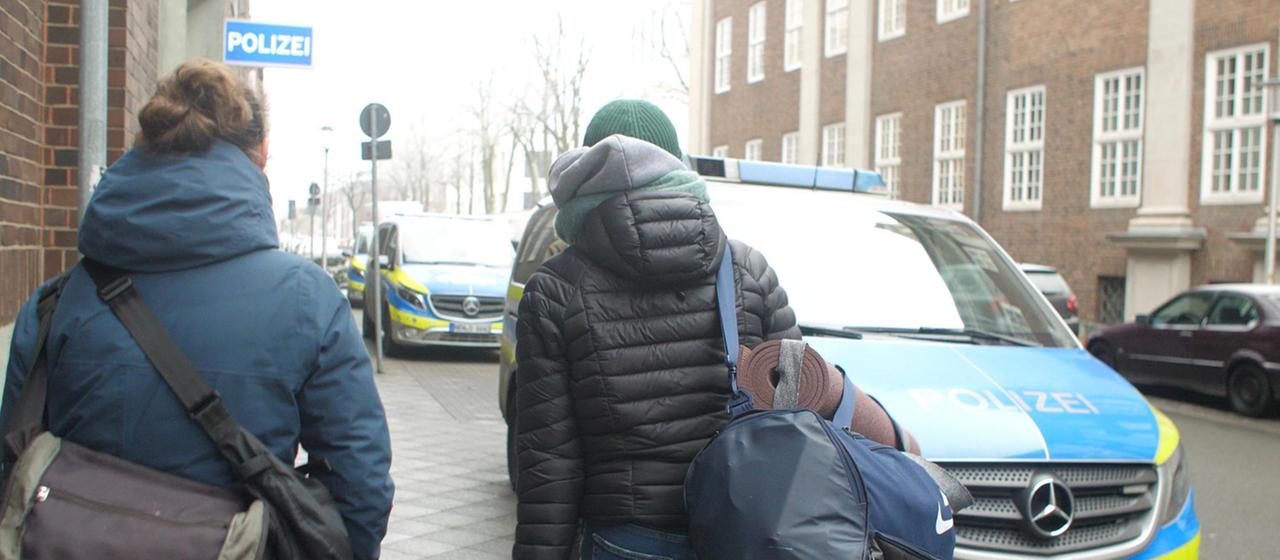 Eine der Verdächtigen und ihre Anwältin gehen eine Straße entlang Richtung Polizeigebäude.