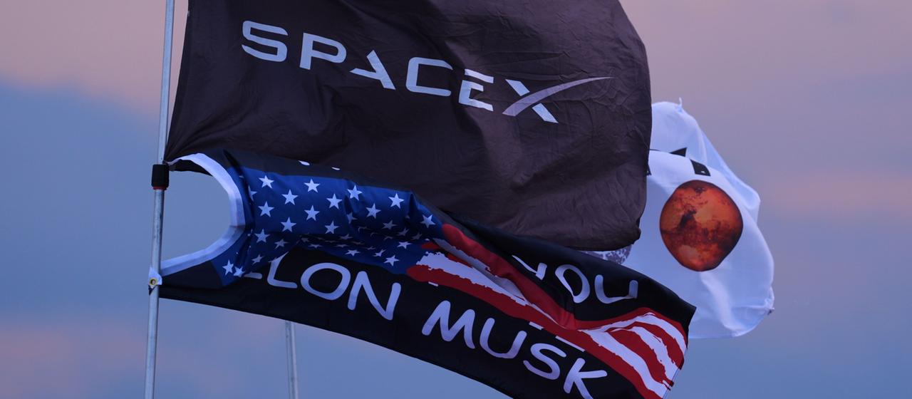 Mehrere Flaggen, darunter zwei mit dem Aufdruck SpaceX und Elon Musk.