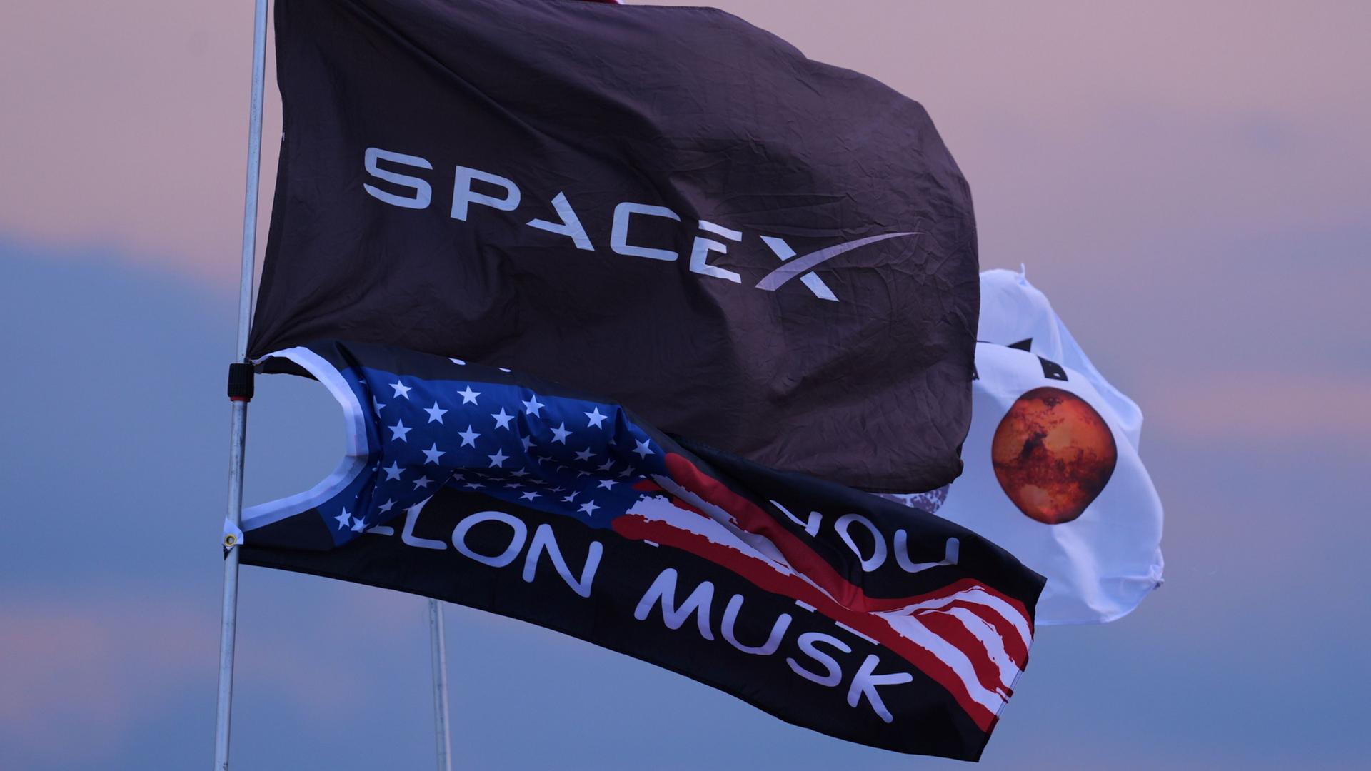 Mehrere Flaggen, darunter zwei mit dem Aufdruck SpaceX und Elon Musk. | Eric Gay/AP/dpa