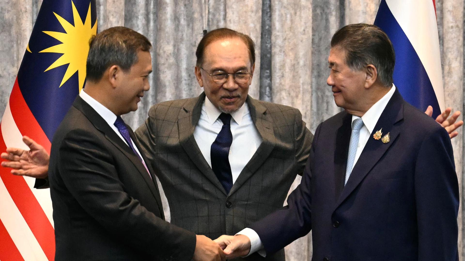 Hun Manet und Phumtham Wechayachai schütteln sich die Hände, während Anwar Ibrahim die Arme ausbreitet. | EPA