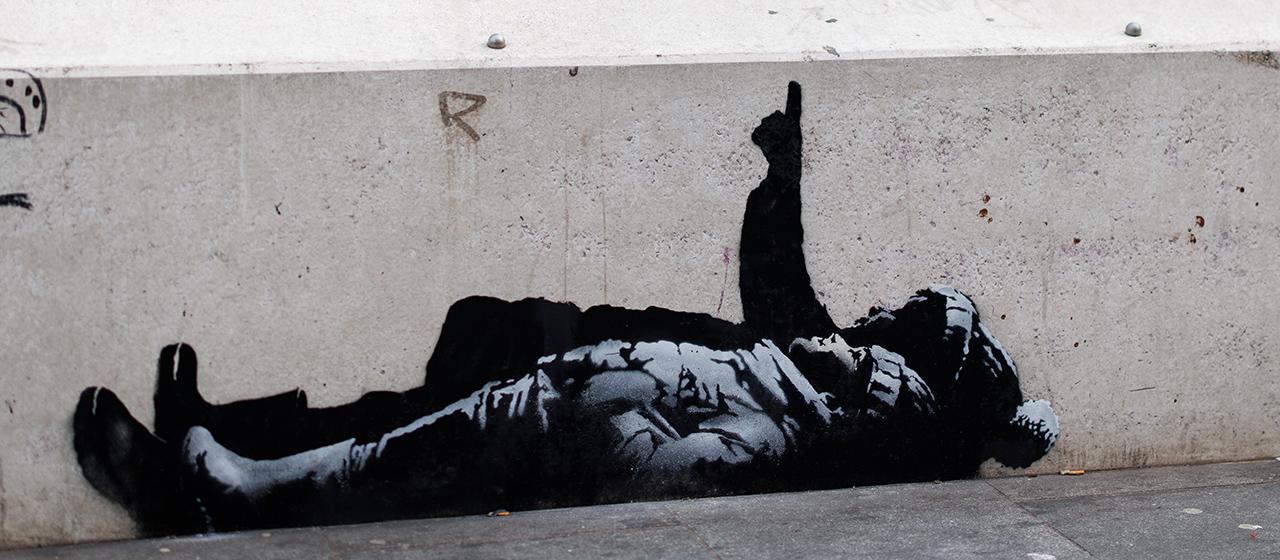 Menschen sitzen hinter einer Mauer, auf der ein Streetartkunstwerk mit zwei liegenden Kindern zu sehen ist.