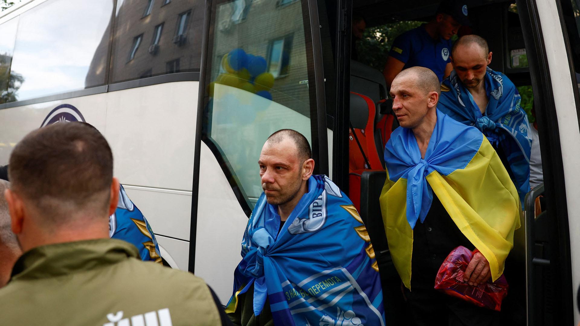 Ukrainische Kriegsgefangene verlassen in ukrainische Flaggen gehüllt einen Bus. | REUTERS