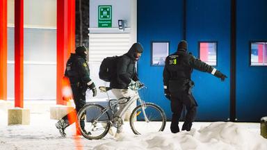 Ein Migrant (M) geht mit einem Fahrrad zwischen Beamten an der finnischen Grenzstation Vartius