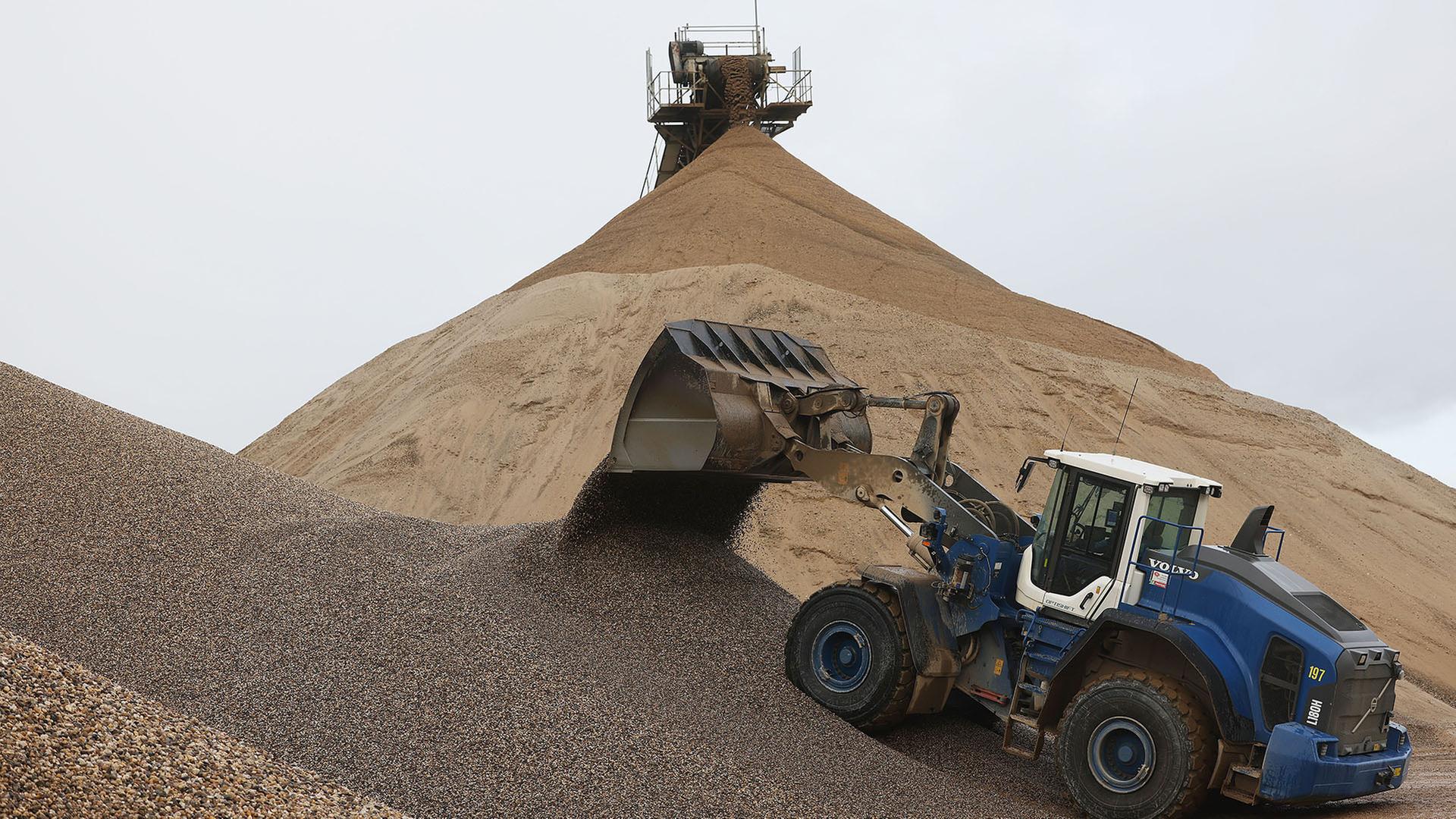 Ein Bagger schaufelt Kies auf eine Halde in einem Kieswerk. | picture alliance/dpa