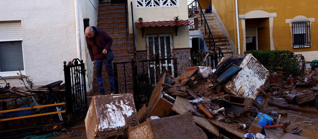 Ein Mann steht vor einem Haus in der spanischen Stadt Utiel. Die Straße ist mit Schlamm und Trümmern übersät.