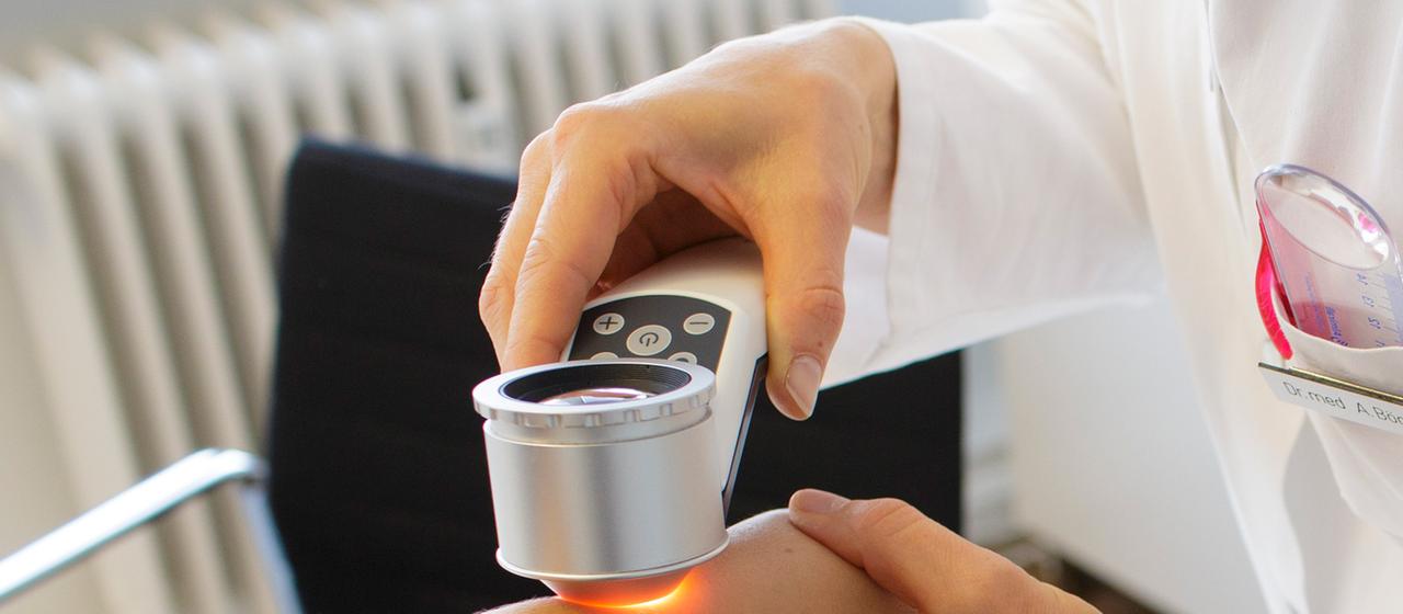 Eine Hautärztin untersucht mit einem speziellen Vergrößerungsglas die Haut einer Patientin bei einer Hautkrebs-Früherkennung.