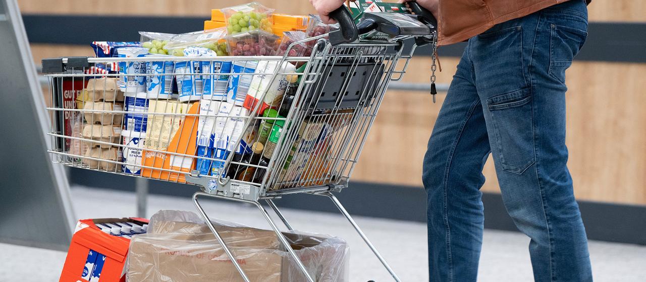 Ein Mann schiebt einen vollen Einkaufswagen mit Lebensmitteln und Getränken.