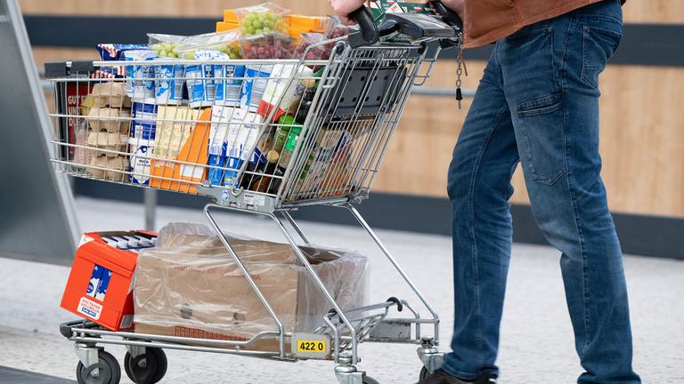 Ein Mann schiebt einen vollen Einkaufswagen mit Lebensmitteln und Getränken.