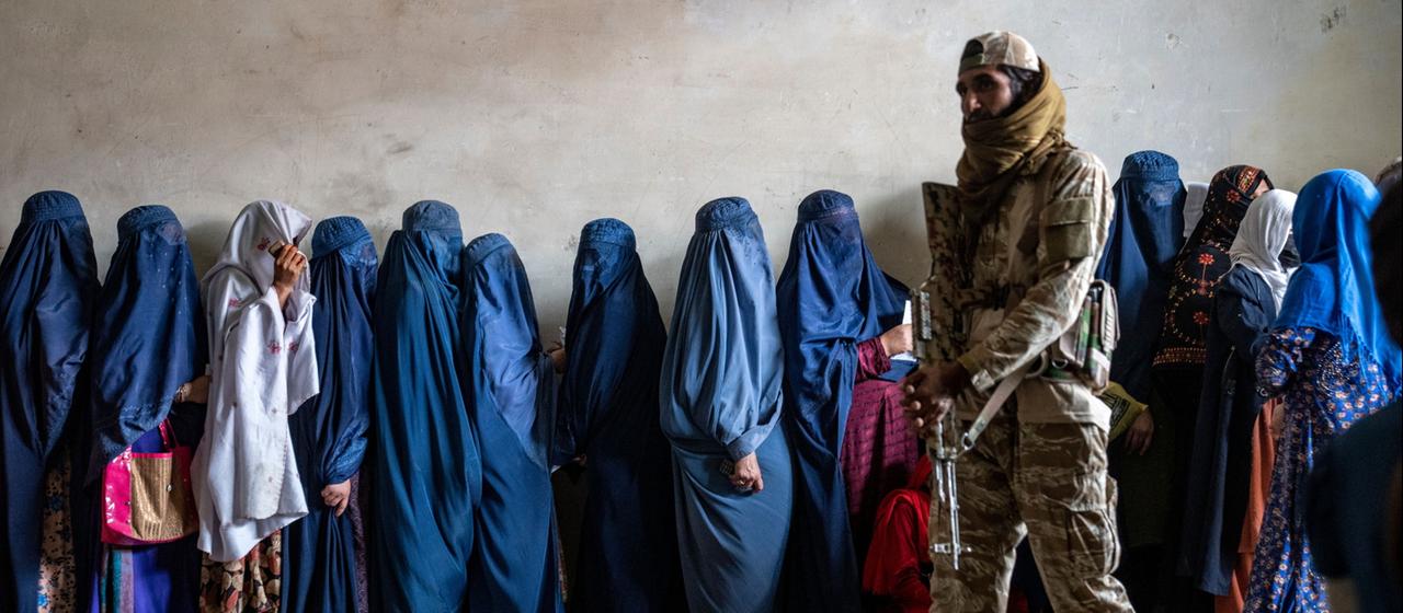 Ein Taliban vor Frauen in Kabul, die auf 2023 Lebensmittelrationen warten.