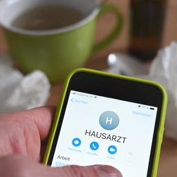 Eine Person hält ein Telefon mit dem Schriftzug "Hausarzt" in den Händen.