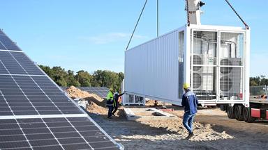 An einem fast fertigen Solarpark des Energieversorgers EnBW wird ein Batteriespeicher angeliefert.