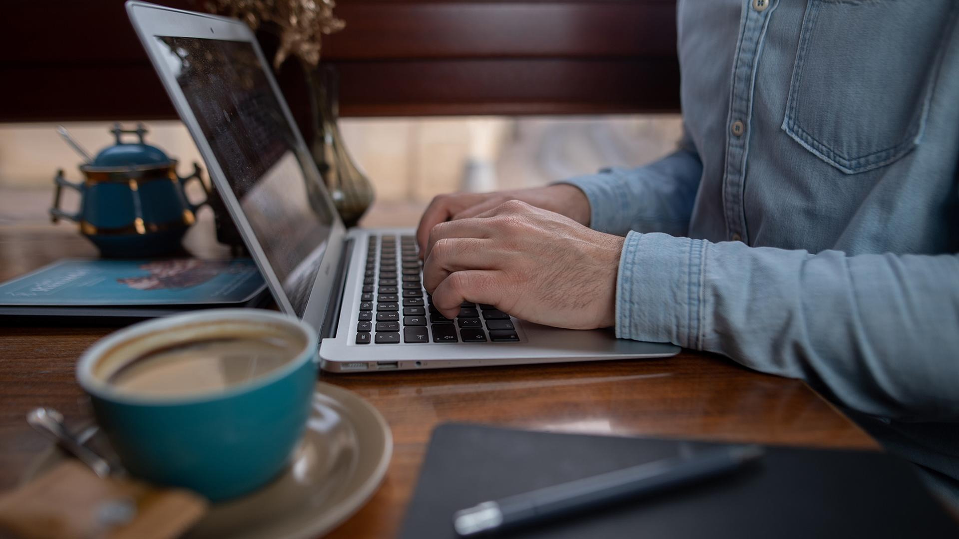 Ein Mann arbeitet in einem Café an einem Laptop. | picture alliance/dpa