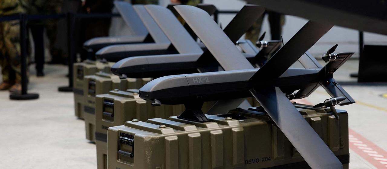 Drohnen vom Typ HX-2 stehen in einer Reihe auf olivgrünen Transportkisten in einer Halle.