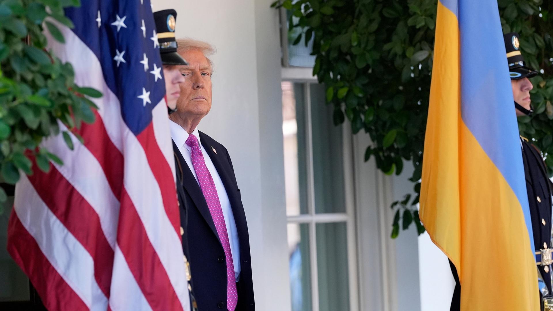US-Präsident Trump steht zwischen einer amerikanischen und einer ukrainischen Flagge. | AP