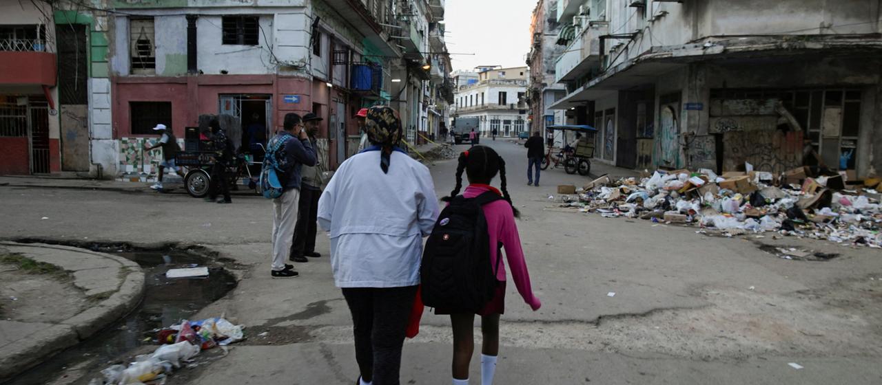 Eine Schülerin und ihre Mutter gehen über verschmutzte Straßen in Havanna.
