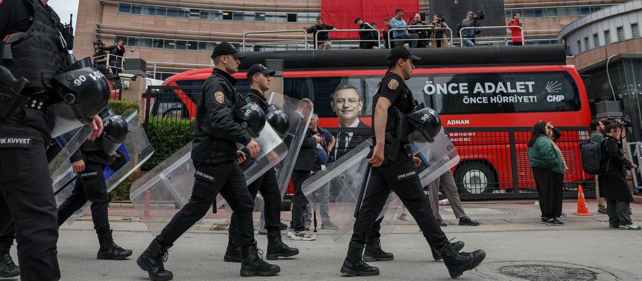 Polizisten marschieren mit Schutzschilden an einem Gebäude mit türkischer Flagge vorbei