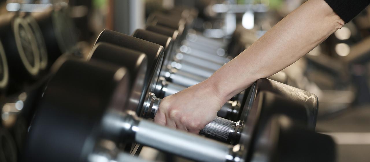 Ein Mensch greift Hanteln in einem Fitnessstudio. | dpa Ein Mensch greift Hanteln in einem Fitnessstudio.