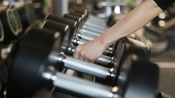 Ein Mensch greift Hanteln in einem Fitnessstudio.